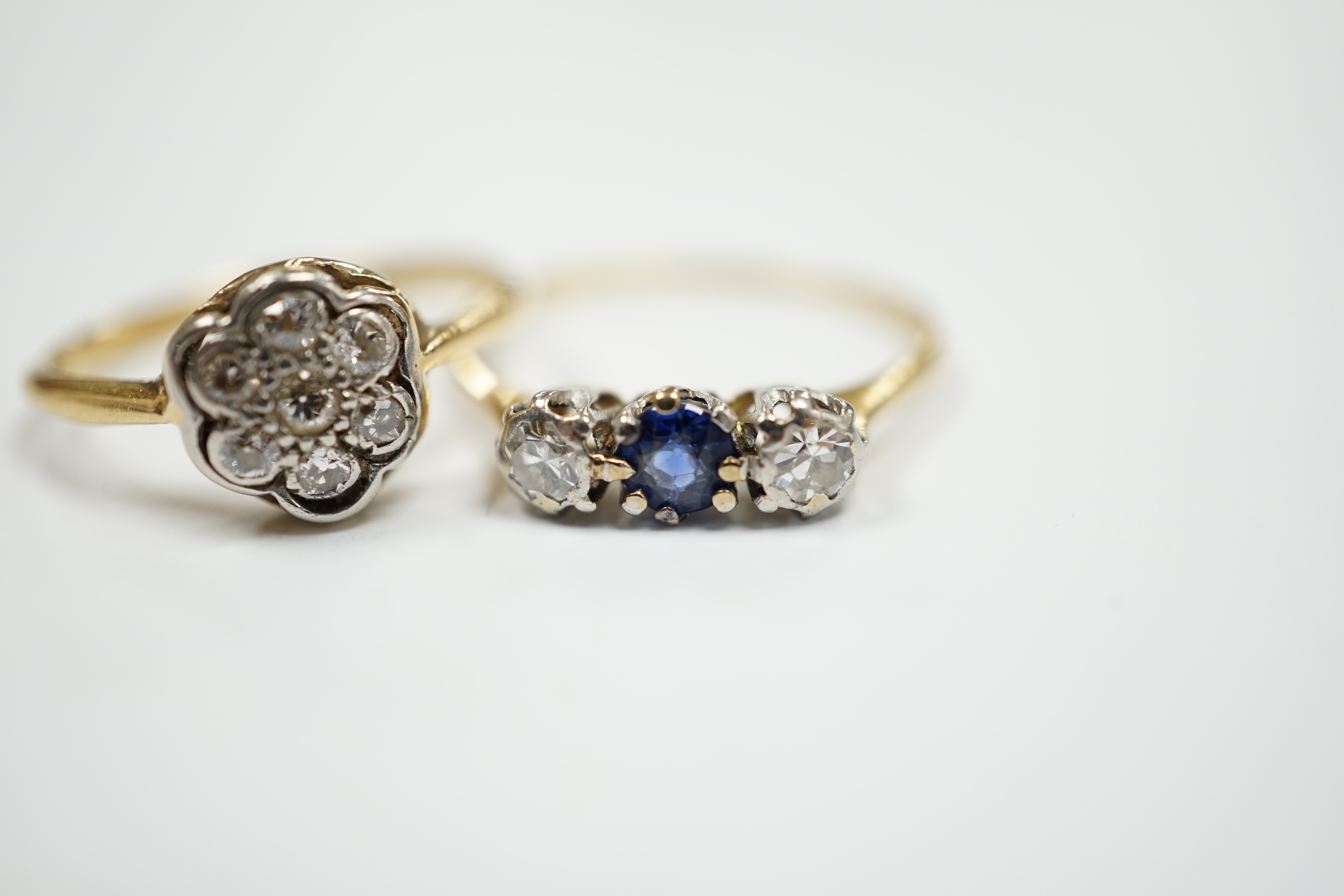 A 1920's 18ct, plat and diamond cluster set flower head ring, size M/N and a 18ct and plat. sapphire and diamond set three stone ring, size O/P, gross 3.9 grams.
